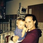 A woman holding a baby in a hospital room with medical equipment.