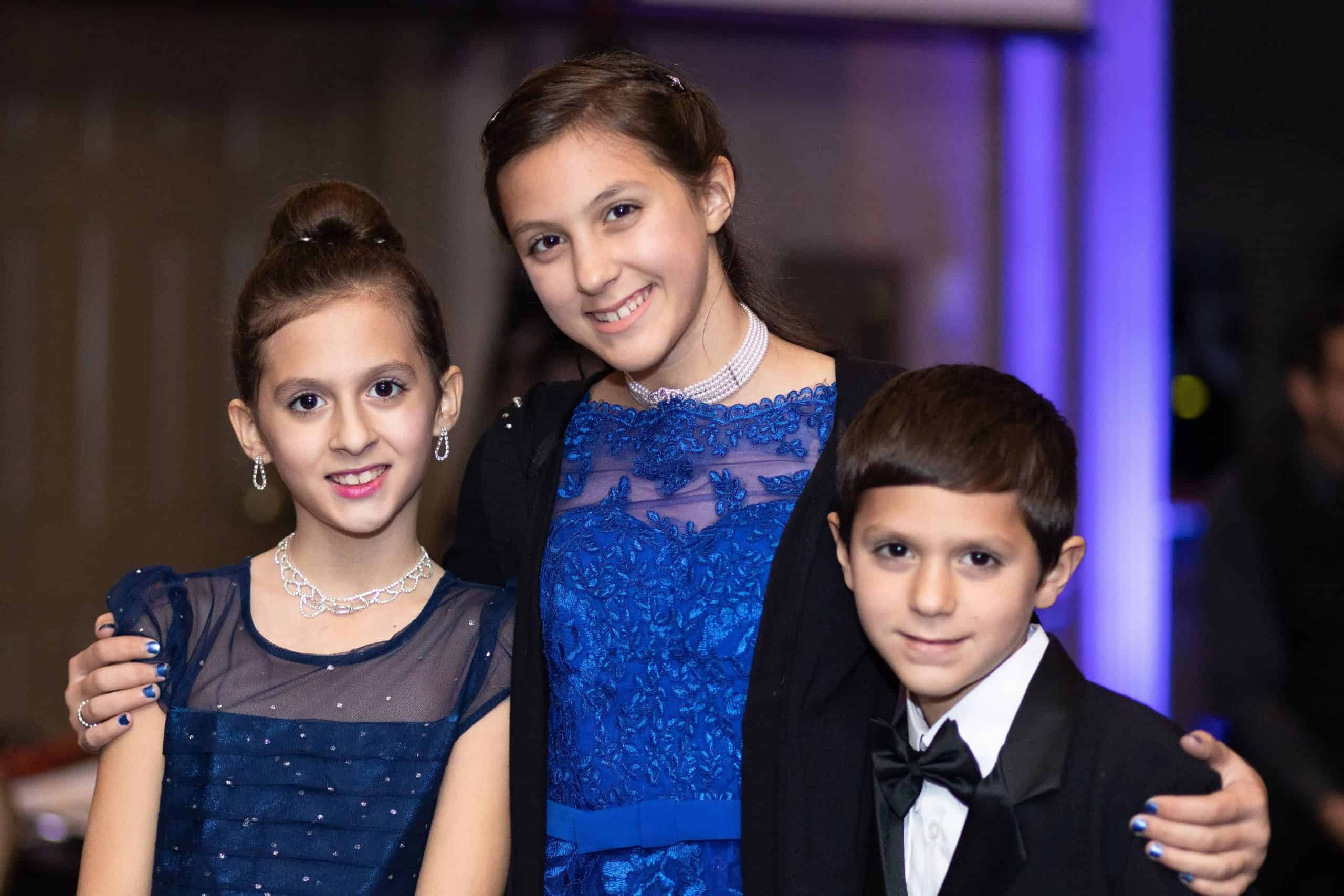 Three well-dressed children smiling at the camera in formal attire.