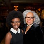 Two smiling women with natural hairstyles in a warmly lit setting.