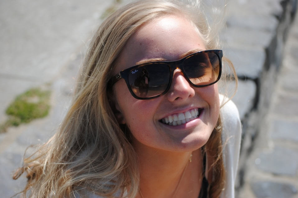 Smiling woman wearing large sunglasses in natural light.