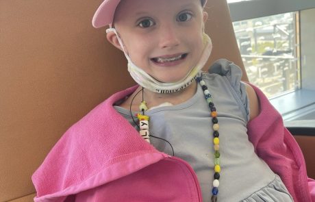 A smiling child wearing a pink jacket and cap indoors.