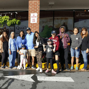 A group of people and children posing outside a store on a sunny day.