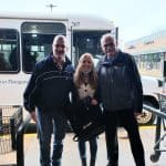 Three people posing outside with buses in the background.
