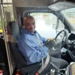Driver seated in a vehicle, smiling at the camera.