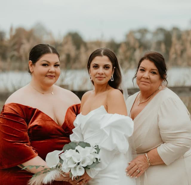 Three women dressed elegantly, with the bride in white holding a bouquet.