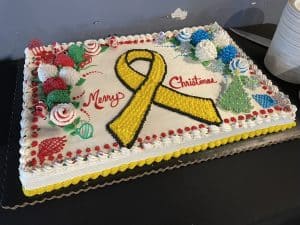 Christmas cake decorated with a yellow awareness ribbon and festive designs.