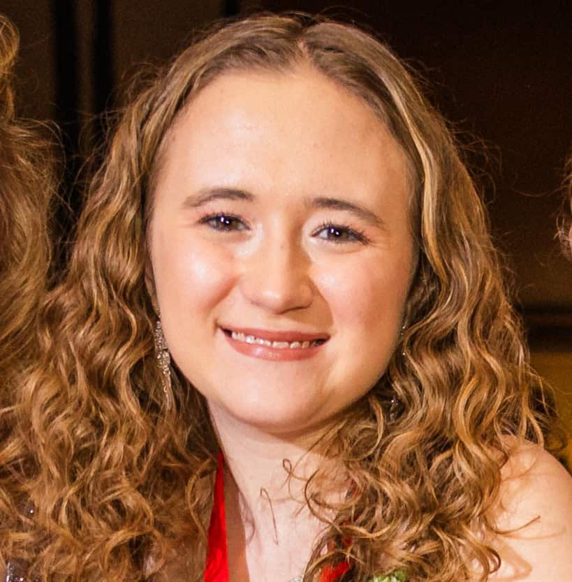 A young woman with curly hair smiling warmly at the camera.