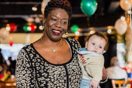 Smiling woman holding a baby at a festive event with balloons.