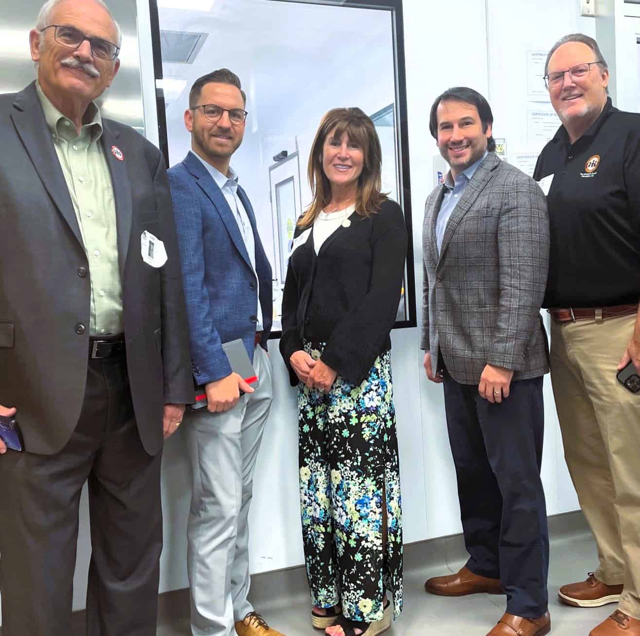Group of five professionals posing indoors near a window.